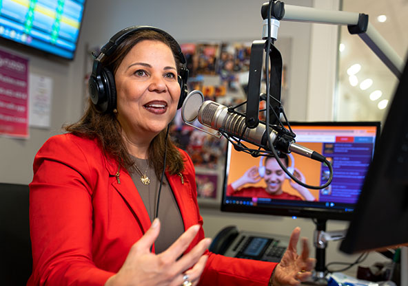 Yvette, a patient at CHRISTUS Health in Tyler, works at a local radio station where she is a DJ. Ivette is speaking on the mix in a red blazer during a show. 