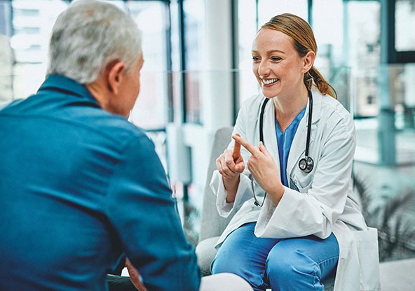 A doctor speaks with a patient in a clinic setting, listening closely and explaining spine surgery options in a calm, supportive conversation.