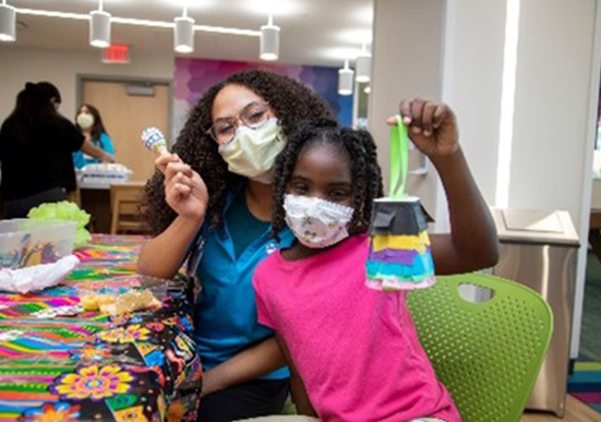 A young girl and her Child Life Specialist show off their crafts