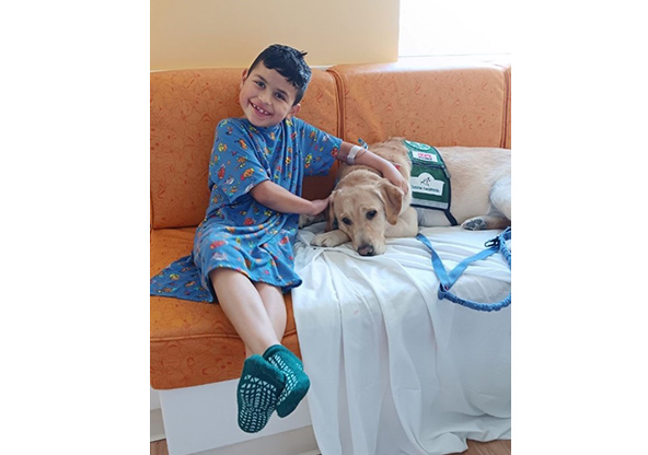 A little boy is hugging a therapy dog who is laying beside him at CHRISTUS Children's