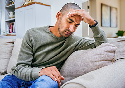 Man sitting on a couch holding his head while suffering a migraine